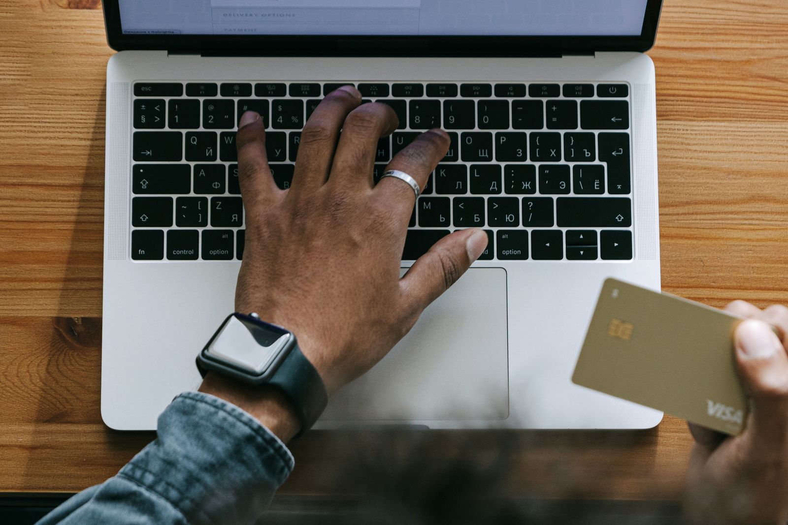 Someone typing on a laptop while holding a payment card during checkout