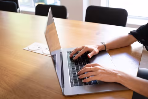 Close-up of hands typing on a laptop at a wooden desk