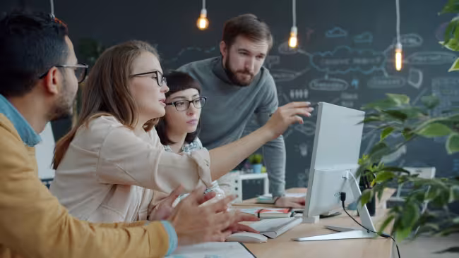 A team gathered around a laptop discussing work in a sprint review meeting